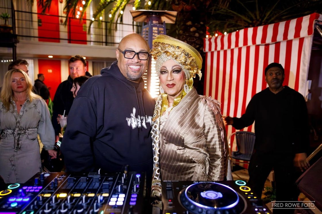 David Harness and Juanita MORE! stand smiling behind at a DJ booth at Phoenix Hotel's New Years Eve party.
